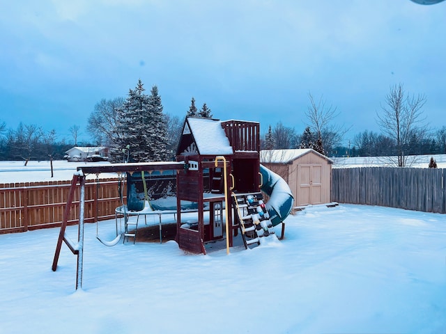 yard layered in snow with an outbuilding, a fenced backyard, a storage shed, and a playground