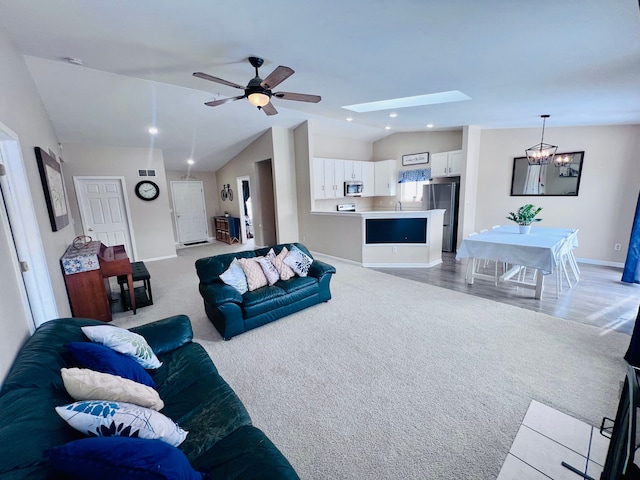 living area featuring light carpet, ceiling fan with notable chandelier, recessed lighting, vaulted ceiling with skylight, and baseboards