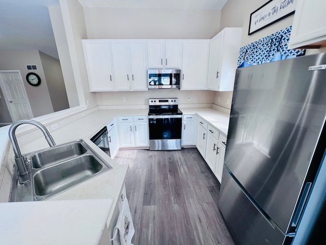 kitchen with a sink, wood finished floors, white cabinetry, appliances with stainless steel finishes, and light countertops