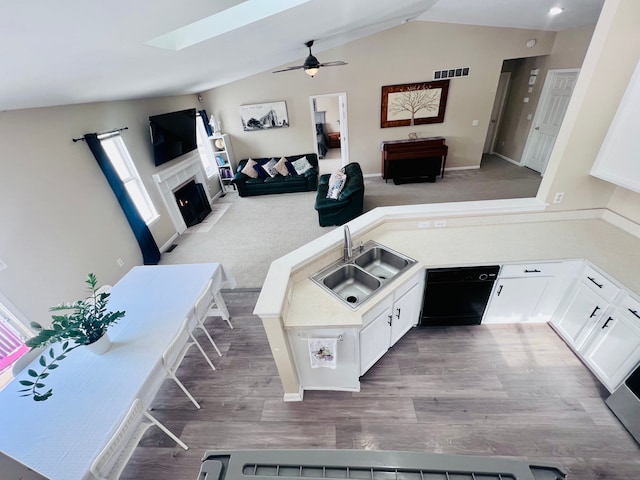 interior space featuring visible vents, a fireplace with flush hearth, a sink, black dishwasher, and vaulted ceiling with skylight