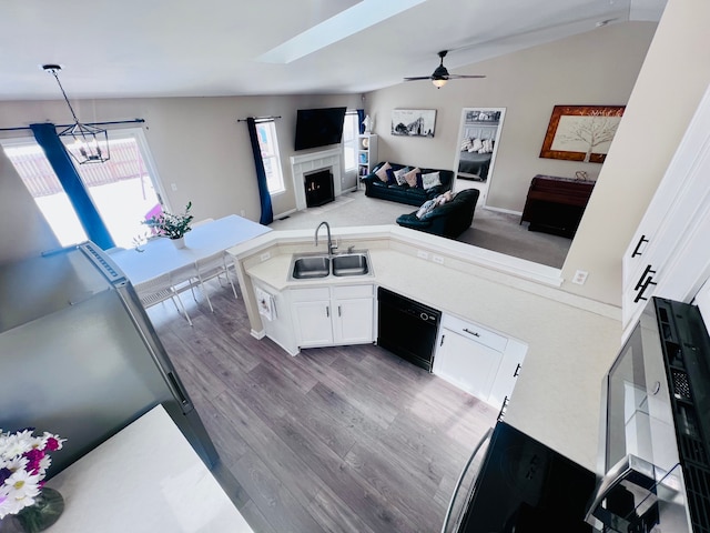 kitchen with a tiled fireplace, a sink, black dishwasher, white cabinetry, and light countertops