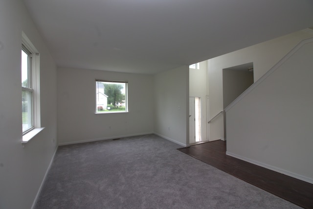 unfurnished room featuring stairway, baseboards, and dark colored carpet