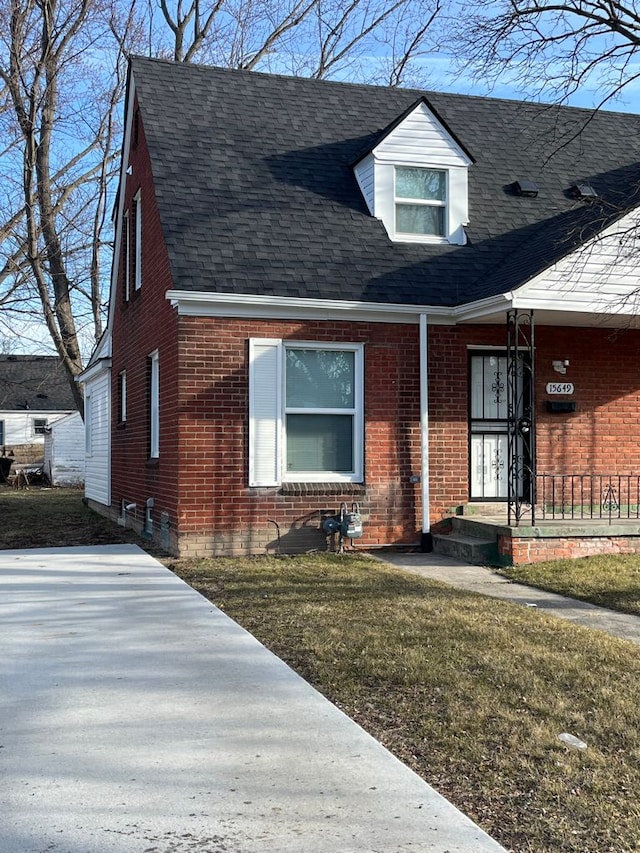 new england style home with brick siding, a front yard, and a shingled roof