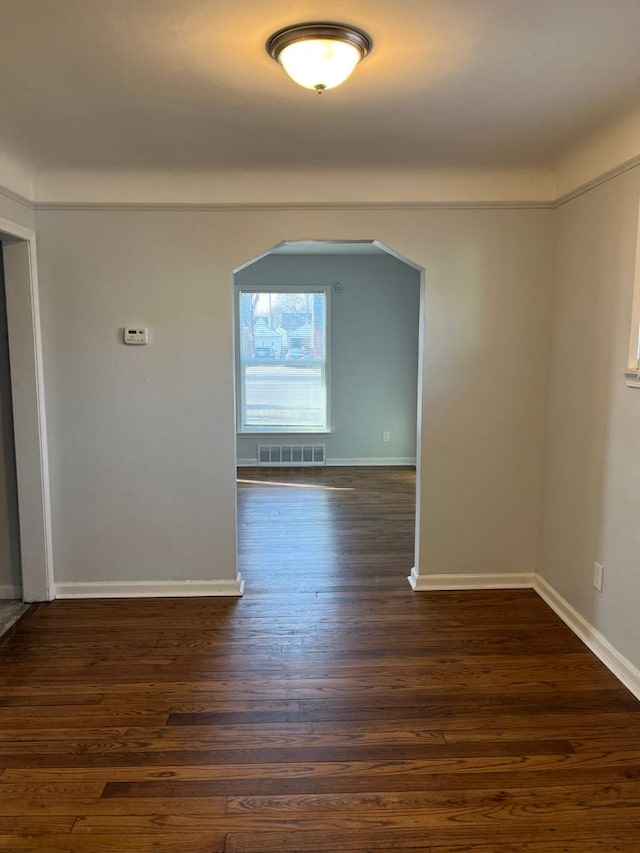 unfurnished room with arched walkways, visible vents, dark wood-style flooring, and baseboards