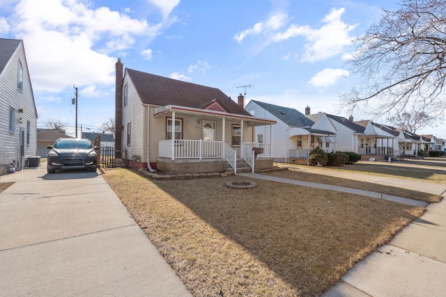 bungalow featuring a residential view, a porch, a chimney, an outdoor structure, and driveway