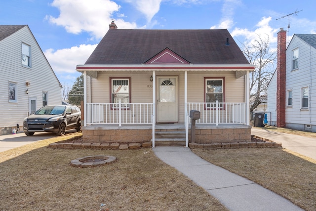 view of front facade featuring covered porch, concrete driveway, a chimney, and roof with shingles