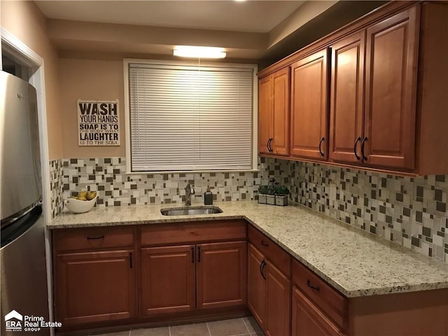 kitchen featuring a sink, tasteful backsplash, freestanding refrigerator, light tile patterned floors, and light stone countertops