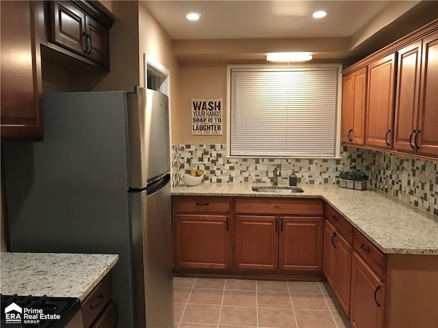 kitchen featuring a sink, tasteful backsplash, light tile patterned floors, and freestanding refrigerator