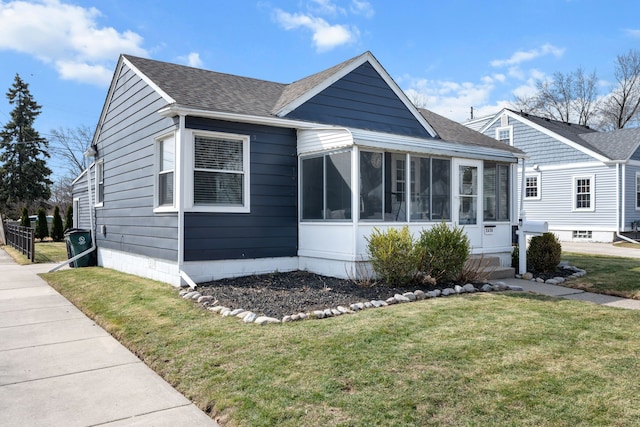 bungalow featuring roof with shingles, a front lawn, and a sunroom