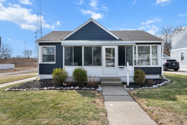 bungalow-style house with a sunroom, a front lawn, and a shingled roof