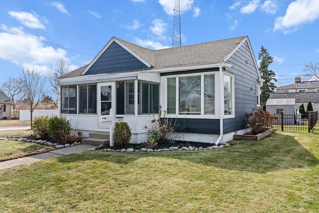 bungalow featuring a front lawn, fence, roof with shingles, and a sunroom