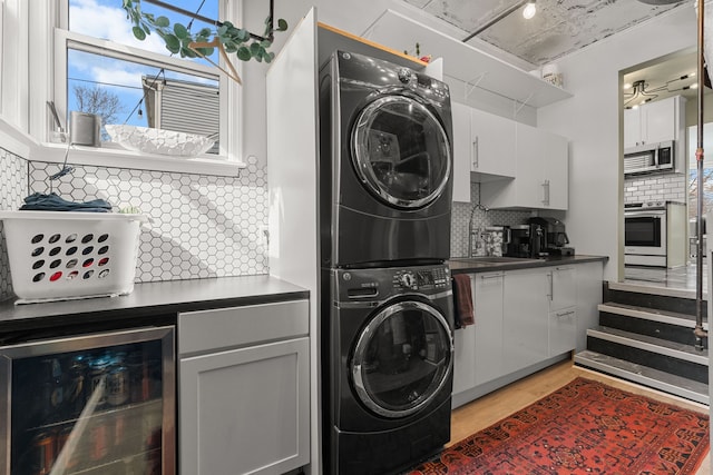 clothes washing area featuring wine cooler, light wood finished floors, stacked washer and clothes dryer, and a sink