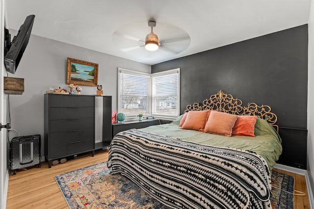 bedroom featuring light wood-style flooring, baseboards, an accent wall, and ceiling fan