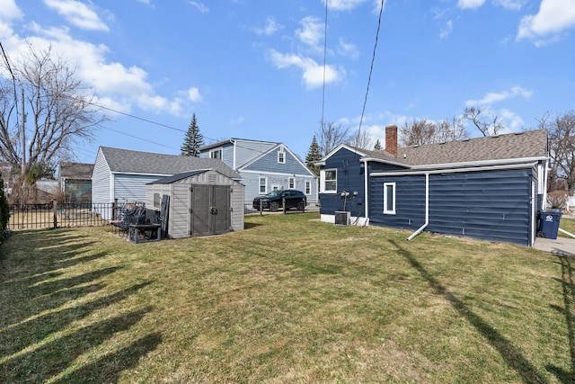 back of property featuring fence, a yard, a chimney, an outdoor structure, and a storage shed