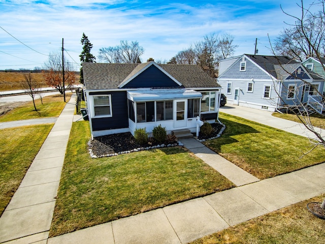 bungalow-style home featuring a shingled roof, a front yard, and a sunroom