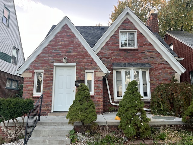 tudor home featuring brick siding and roof with shingles