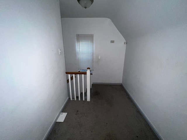 corridor with an upstairs landing, carpet flooring, baseboards, and lofted ceiling