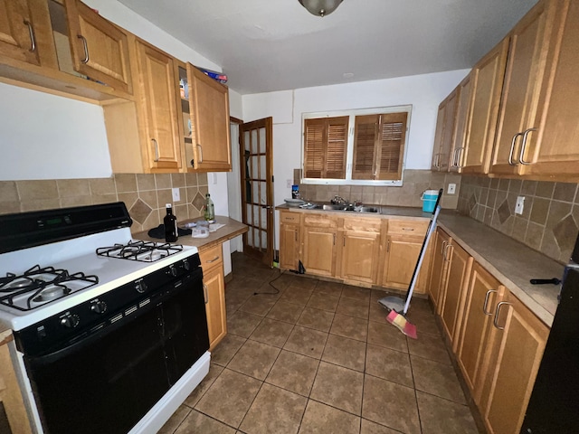 kitchen featuring dark tile patterned floors, a sink, range with gas cooktop, light countertops, and decorative backsplash