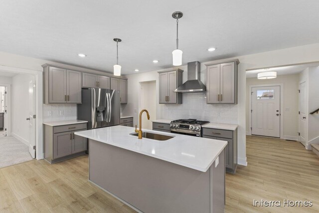 kitchen featuring wall chimney range hood, light countertops, gray cabinets, appliances with stainless steel finishes, and a sink