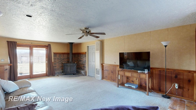 living room featuring a textured ceiling, a wood stove, a ceiling fan, and carpet floors