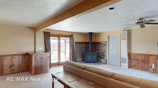 living area with a wainscoted wall, a wood stove, ceiling fan, a textured ceiling, and light carpet