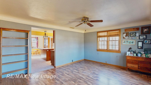 empty room with ceiling fan, visible vents, baseboards, and wood finished floors