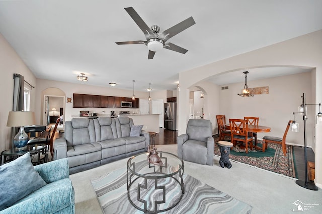 living area featuring arched walkways, visible vents, a ceiling fan, and dark colored carpet