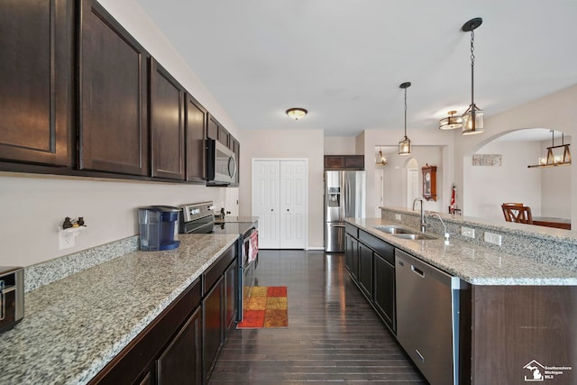 kitchen featuring dark brown cabinets, dark wood finished floors, arched walkways, stainless steel appliances, and a sink