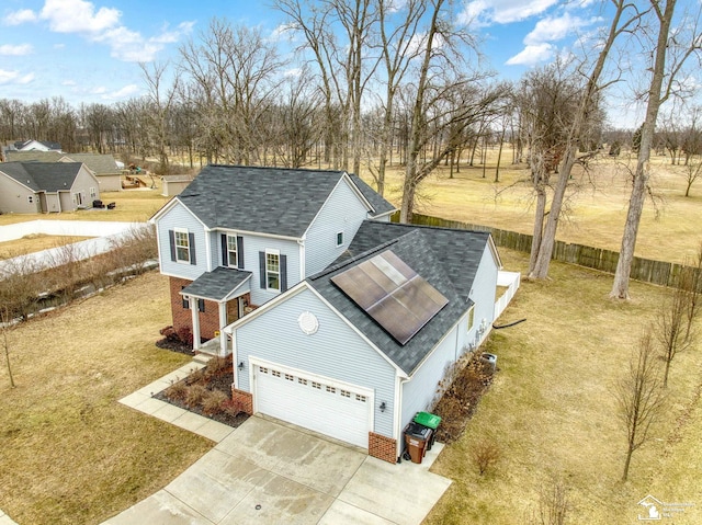 view of front of home featuring fence, concrete driveway, an attached garage, brick siding, and solar panels