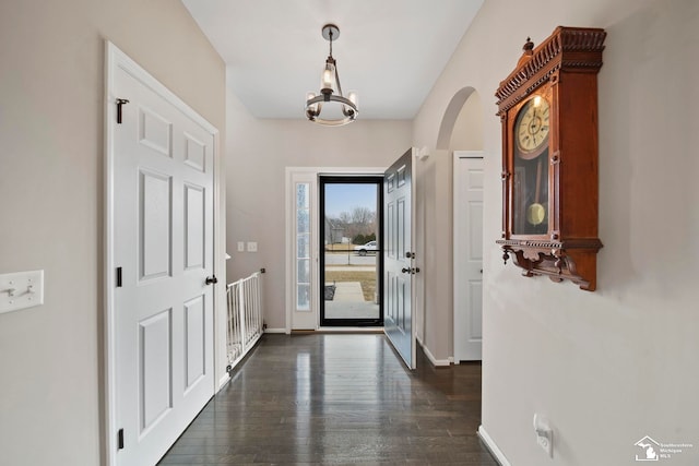 foyer entrance featuring a notable chandelier, baseboards, dark wood-style flooring, and arched walkways