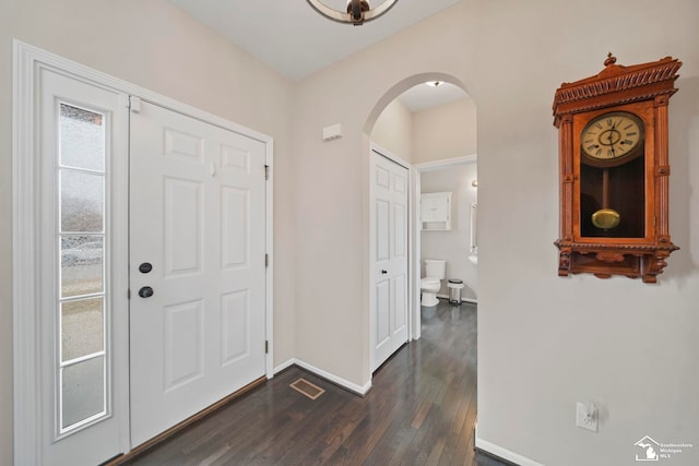 entryway with dark wood-type flooring, baseboards, arched walkways, and visible vents