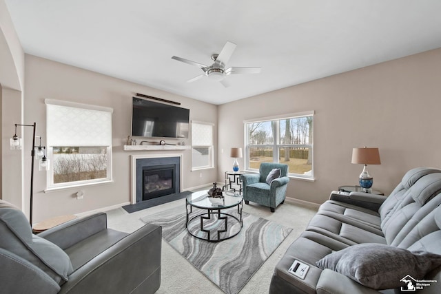 carpeted living room with ceiling fan, baseboards, and a glass covered fireplace