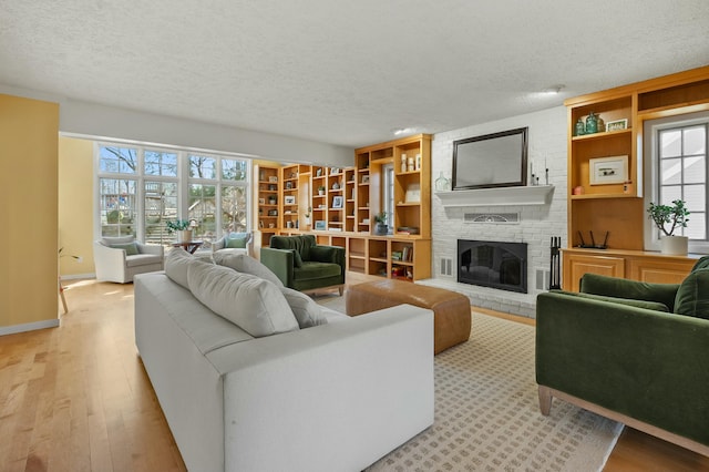 living room featuring baseboards, a textured ceiling, a fireplace, and light wood finished floors