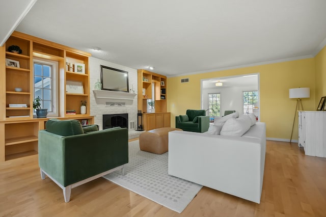 living area with built in shelves, baseboards, light wood finished floors, a fireplace, and ornamental molding