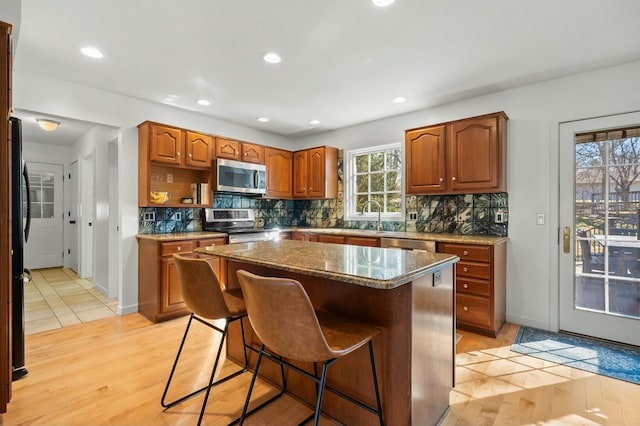 kitchen featuring tasteful backsplash, brown cabinets, appliances with stainless steel finishes, and light wood-style floors