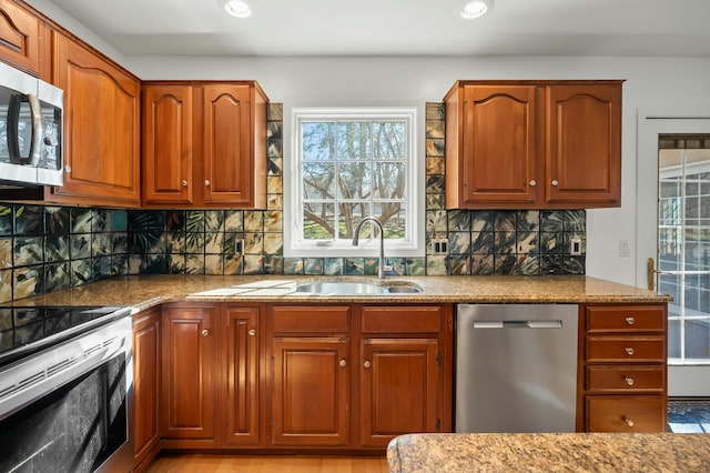 kitchen with brown cabinets, a sink, tasteful backsplash, stainless steel appliances, and stone counters