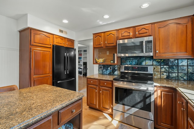 kitchen with visible vents, dark stone countertops, appliances with stainless steel finishes, brown cabinetry, and decorative backsplash