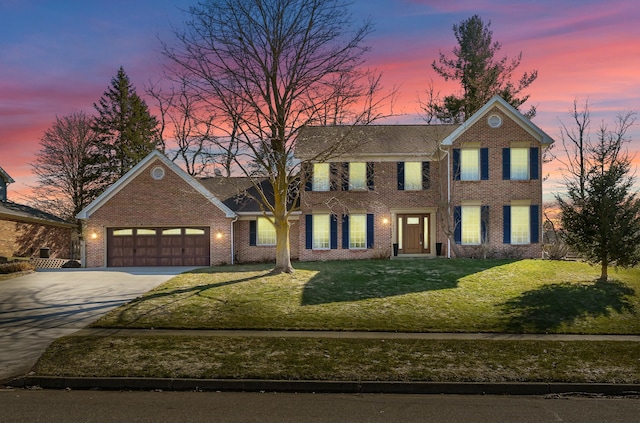 colonial inspired home with brick siding, a garage, driveway, and a yard