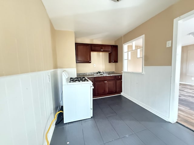 kitchen with a sink, a wainscoted wall, white gas range, and light countertops