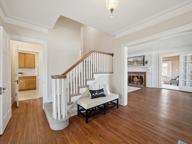 staircase with a glass covered fireplace, wood finished floors, and ornamental molding