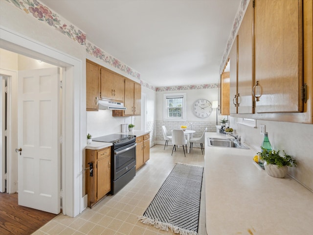 kitchen with brown cabinetry, stainless steel electric range, a sink, light countertops, and under cabinet range hood