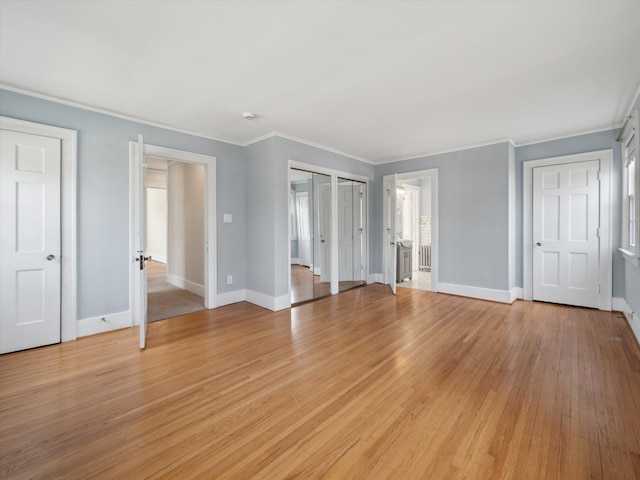 unfurnished bedroom featuring baseboards, light wood-style flooring, radiator heating unit, multiple closets, and crown molding