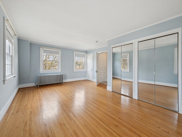 unfurnished bedroom featuring light wood-type flooring, multiple closets, radiator heating unit, crown molding, and baseboards