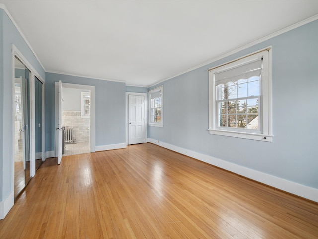 unfurnished bedroom featuring radiator, multiple windows, baseboards, and light wood finished floors