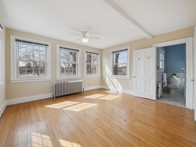 spare room featuring beam ceiling, a wealth of natural light, radiator, and light wood finished floors