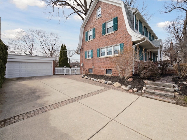 view of side of property featuring a gambrel roof, an outbuilding, fence, a garage, and brick siding