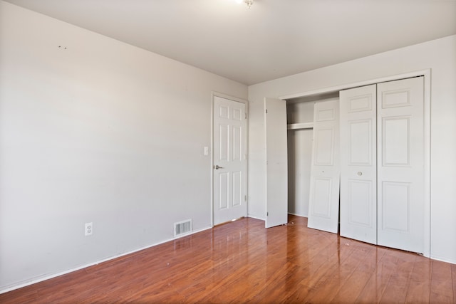 unfurnished bedroom with wood finished floors, visible vents, and a closet