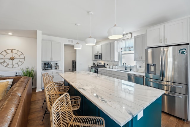 kitchen with a sink, a kitchen breakfast bar, dark wood finished floors, a center island, and appliances with stainless steel finishes