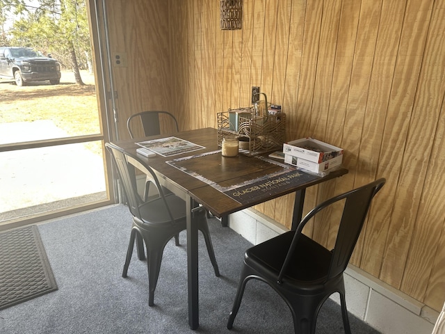 carpeted dining area featuring wood walls and a healthy amount of sunlight