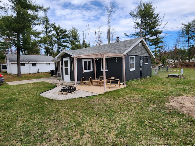 rear view of property featuring a lawn, a shingled roof, a fire pit, and a patio area